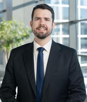 man with short dark hair and beard wearing a dark suit and tie with a white shirt
